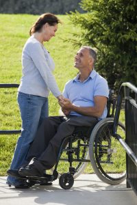 Woman holding man's hand in a wheelchair.