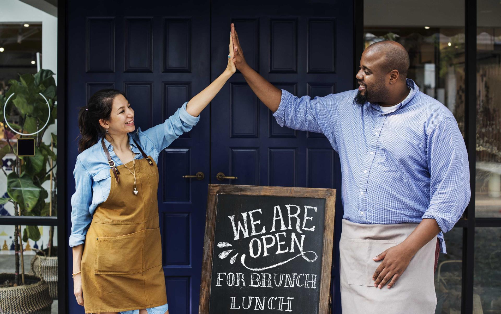 Woman and man high fiving in front of open sign